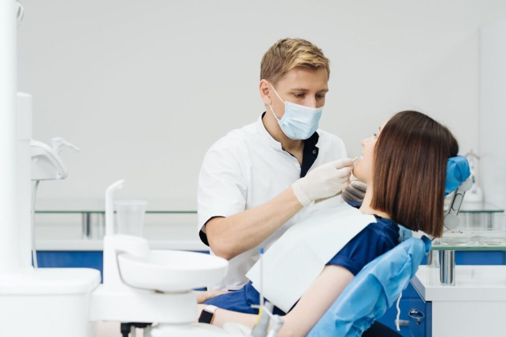 close up portrait beautiful young lady sitting dental chair while stomatologist hands sterile gloves holding tooth samples