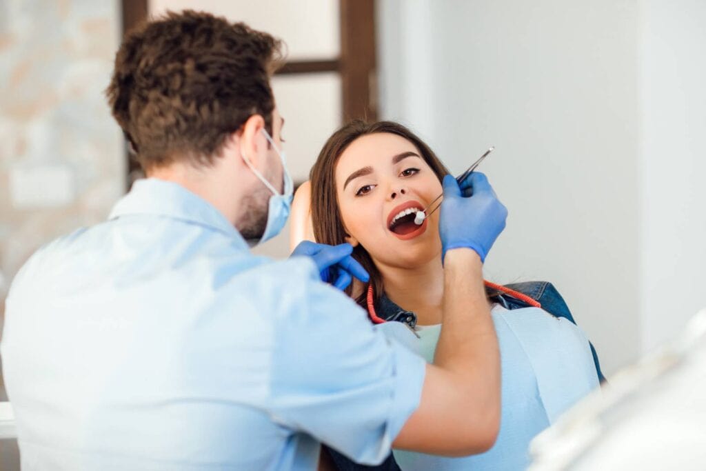 dentist making professional teeth cleaning withb cotton female young patient dental office