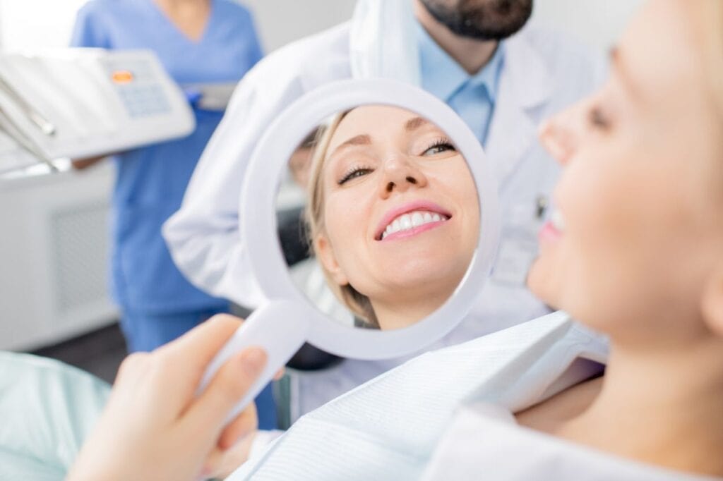 reflection mirror healthy smile pretty young smiling female patient dental clinics after whitening teeth procedure by her dentist